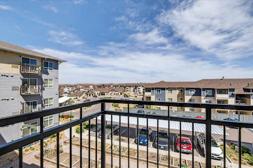 A balcony view of a parking lot with cars and apartment buildings.
