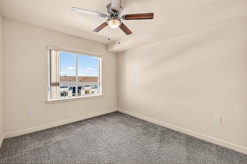 A room with a ceiling fan and a window overlooking a residential area.