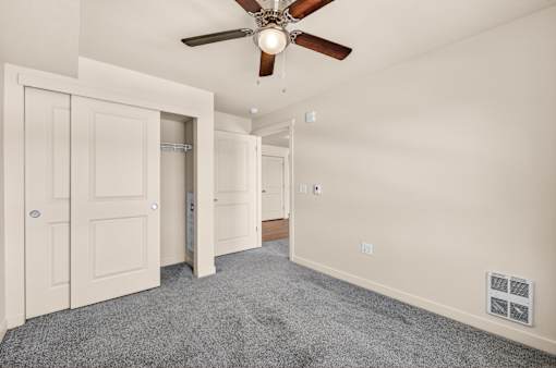 A room with a ceiling fan and a grey carpet.