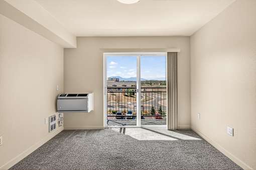 A room with a sliding glass door leading to a balcony with a view of the city.