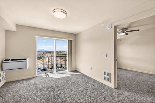 A well-lit room with a sliding glass door leading to a balcony.