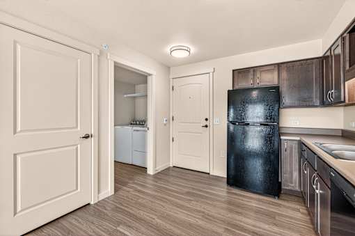 A kitchen with a black fridge and wooden floors.