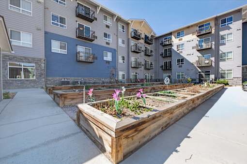 A long wooden planter box with flowers in front of apartment buildings.