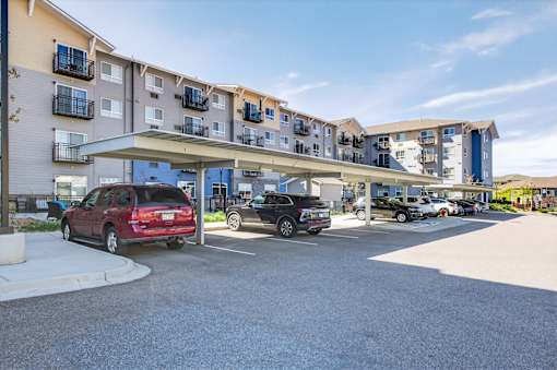 A red car is parked in a parking lot in front of apartment buildings.