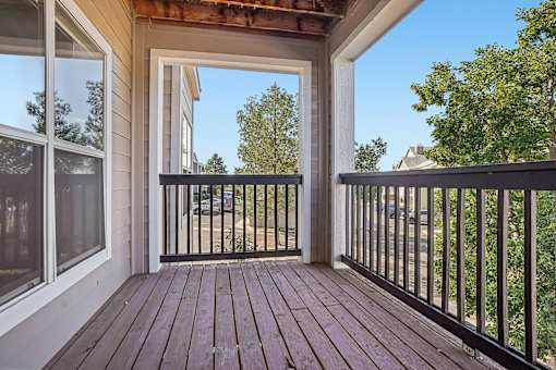 A wooden deck with a black railing and a glass door leading to a patio.