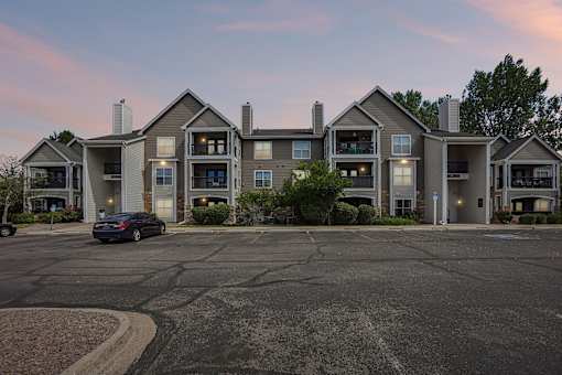 A car is parked in front of a building with a parking lot in front.