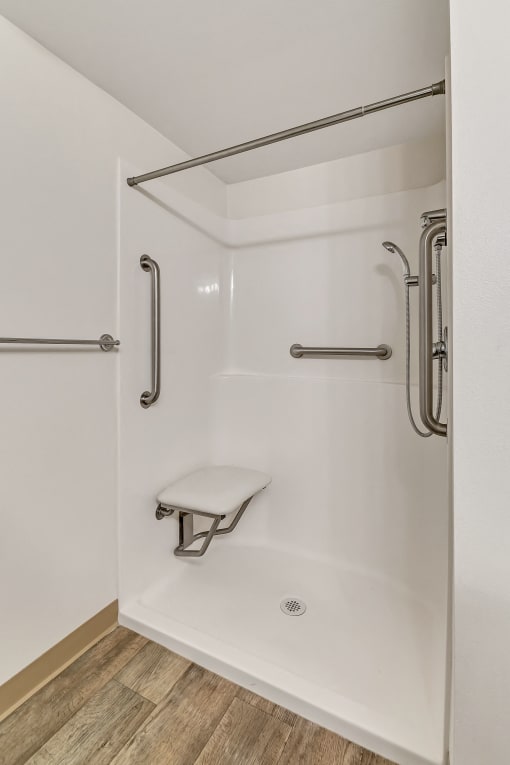 a white shower with grab bars and a stool in a bathroom