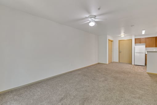 an empty living room with a kitchen and a ceiling fan