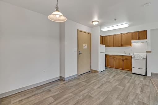 the living room and kitchen of an apartment with wood flooring and white appliances
