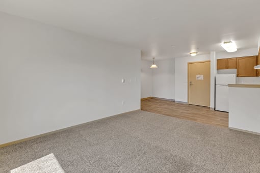 the living room and kitchen of an apartment with white walls and wood flooring
