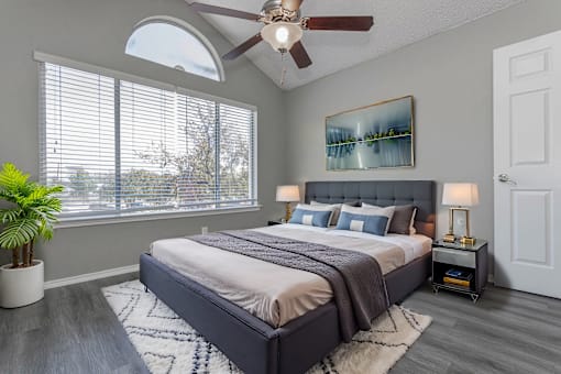 A bedroom with a large bed, a ceiling fan, and a painting on the wall.