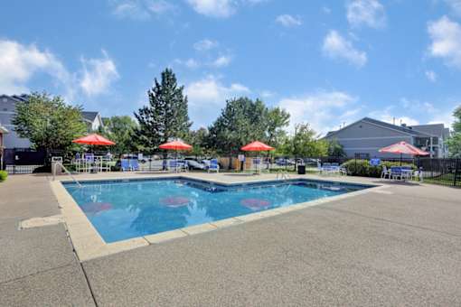 A large outdoor swimming pool with red umbrellas and a slide.