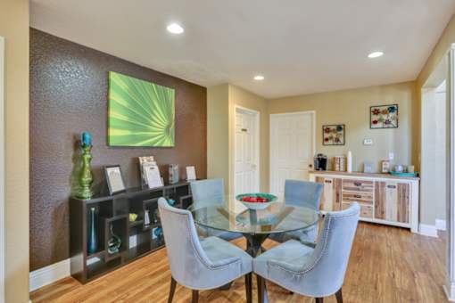 A dining room with a glass table and grey chairs.