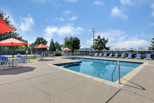 A pool area with red umbrellas and blue chairs.