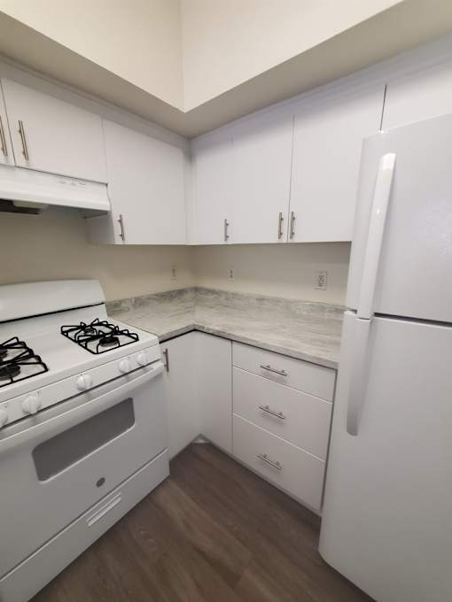 A white kitchen with a stove, refrigerator, and cabinets.