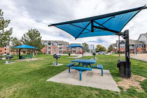 A blue picnic table is under a blue canopy in a park.