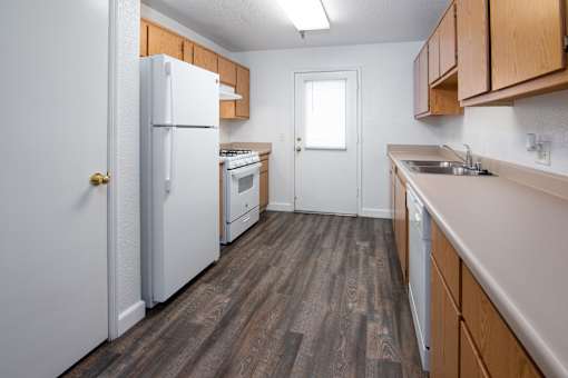 A kitchen with a white refrigerator, wooden cabinets, and a white door.