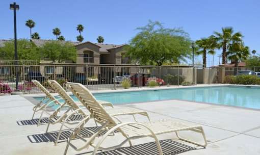 A pool with sun loungers in front of a building with a fence.