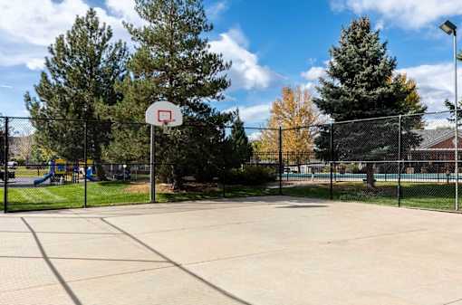A basketball court surrounded by a fence with trees in the background.