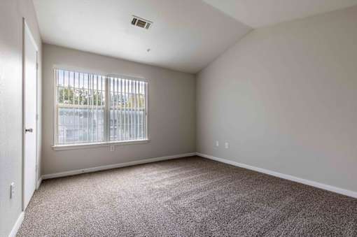 A room with a carpeted floor and a window with blinds.