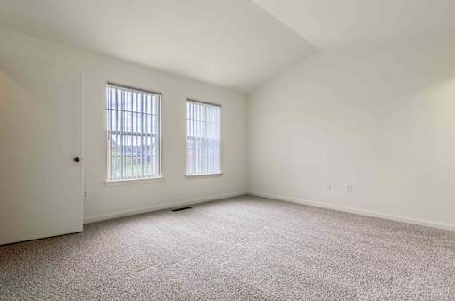 A room with carpeted floor, two windows, and a door.