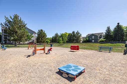 A playground with a blue sandbox in the foreground and a red slide in the background.