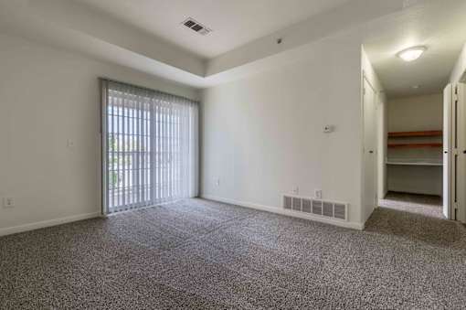 A large, empty room with a carpeted floor and a sliding glass door leading outside.