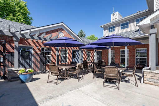 A patio with chairs and umbrellas is set against a brick building.