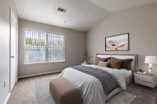 A bedroom with a large bed, a nightstand, and a window with blinds.