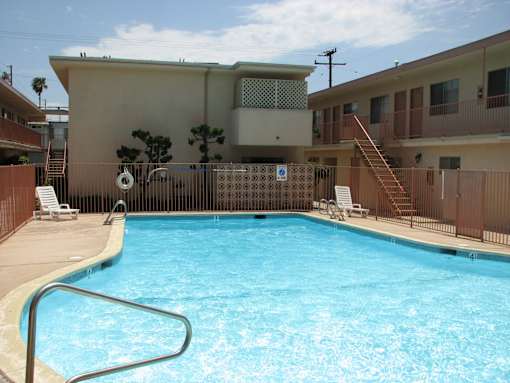 A pool in a residential area with a brown fence and a building in the background.