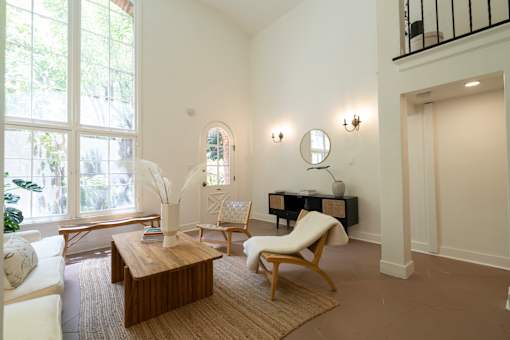 A living room with a white sofa, a wooden chair, a coffee table, and a large window.