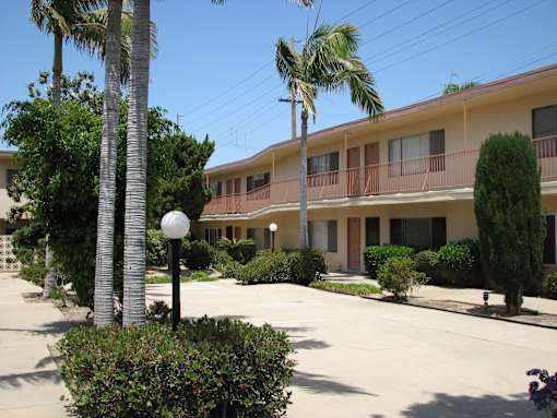 A street view of a residential area with apartment buildings and palm trees.