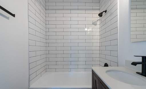 A white tiled bathroom with a white tub and sink.