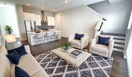 A modern living room with a kitchen area in the background.