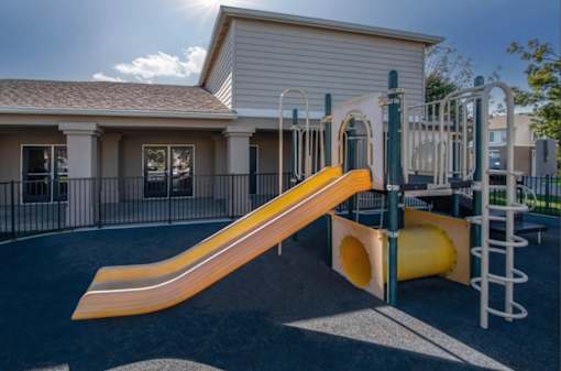 A playground with a yellow slide and a green and white climbing frame.
