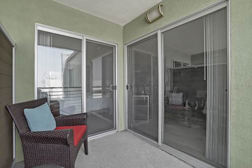A chair with a red cushion and a blue pillow is in front of a glass door.