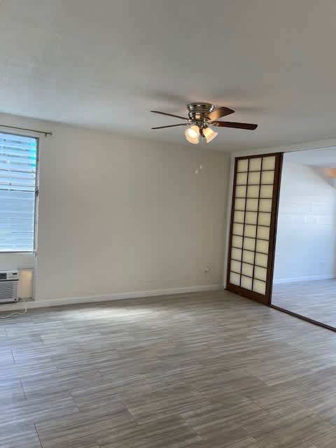 A room with a ceiling fan and light fixture, a window with blinds, and a wooden floor.
