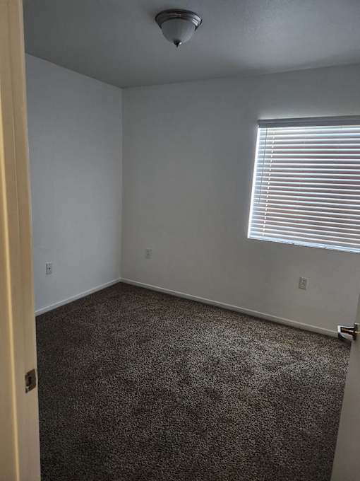 A room with a carpeted floor and a window with blinds.