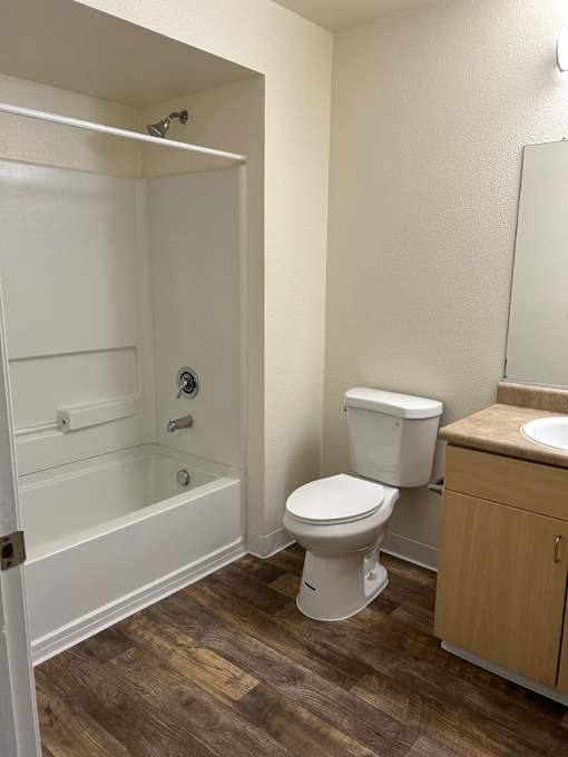 A white toilet is installed in a bathroom with wood flooring.