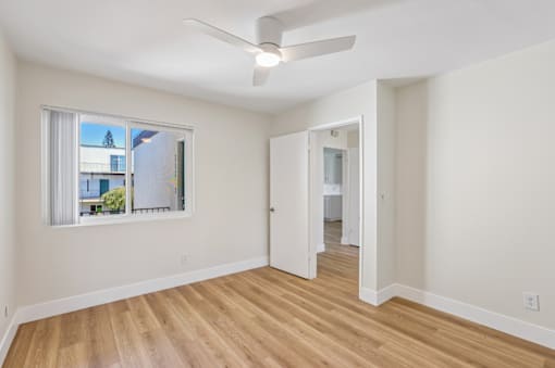 A room with a ceiling fan and a window overlooking a city.