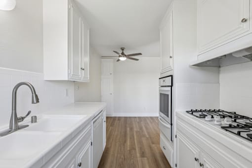 A white kitchen with wood floors and a ceiling fan.