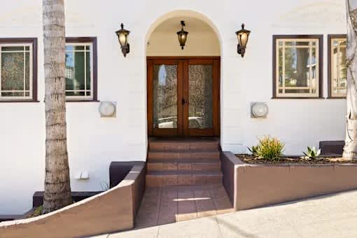 A white house with a brown door and a palm tree in front.