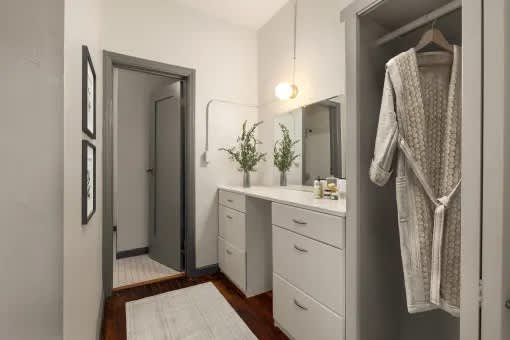 A white bathroom with a mirror, sink, and robe hanging.