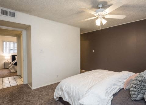 A bedroom with a bed, ceiling fan, and a doorway leading to another room.