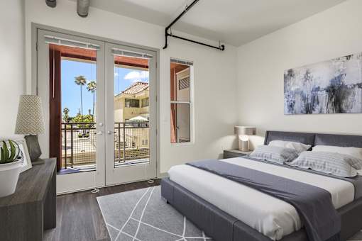 A bedroom with a large bed and a view of a balcony through the window.