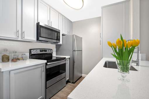 A kitchen with a white counter top and a vase of yellow tulips.