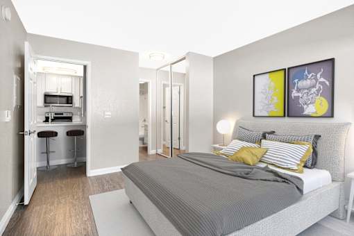 A bedroom with a bed, a mirror, and a small kitchen area.