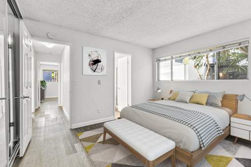 A bedroom with a bed, bench, and a fridge.