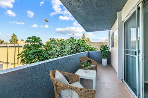 A balcony with a table and chairs overlooking a tree-filled area.