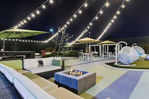 A patio with a fire pit and seating area under string lights.